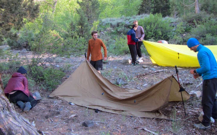 a group of outward bound students work to set up tarp shelters 